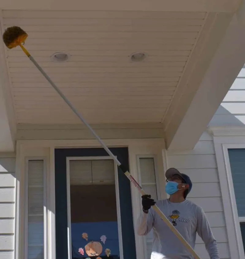 Pest control technician performing dewebbing service on a residential porch