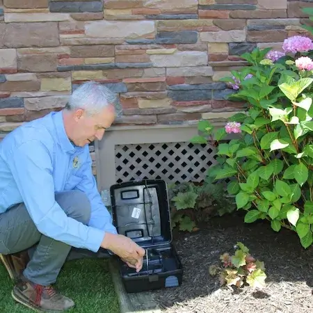Rodent bait station anchored along foundation
